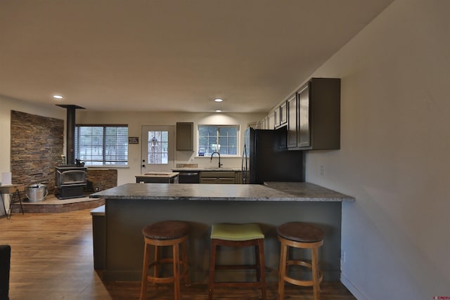 kitchen with sink, a wood stove, dark hardwood / wood-style flooring, kitchen peninsula, and black appliances