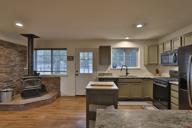 kitchen with sink, light stone counters, light wood-type flooring, a wood stove, and black appliances