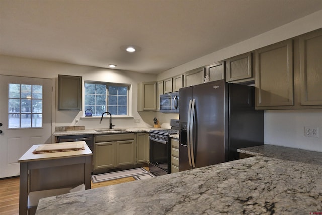 kitchen featuring stainless steel refrigerator with ice dispenser, sink, light stone counters, and black gas range