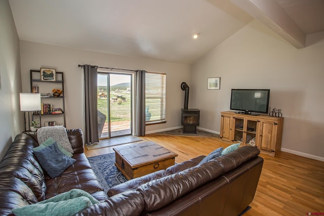 living room featuring a wood stove, vaulted ceiling with beams, and light wood-type flooring