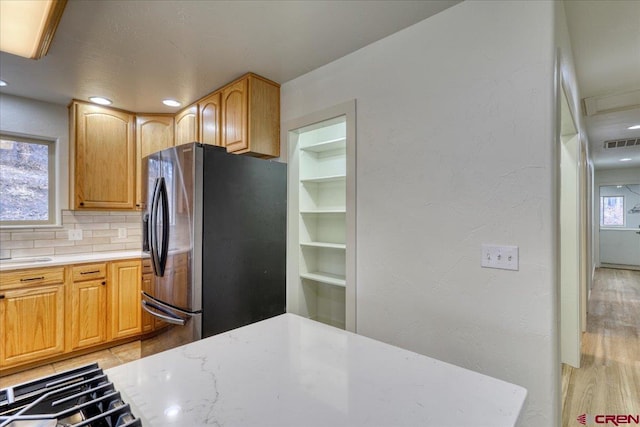 kitchen featuring stovetop, a wealth of natural light, stainless steel fridge, and decorative backsplash