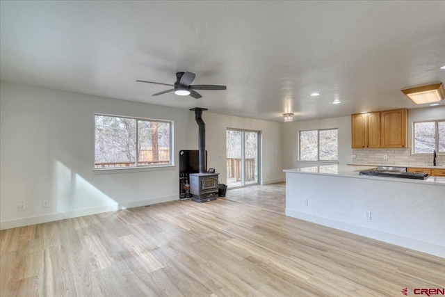 kitchen with a wood stove, decorative backsplash, ceiling fan, and light hardwood / wood-style flooring