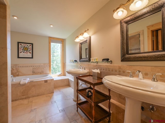 bathroom with double sink, tiled bath, and tile walls