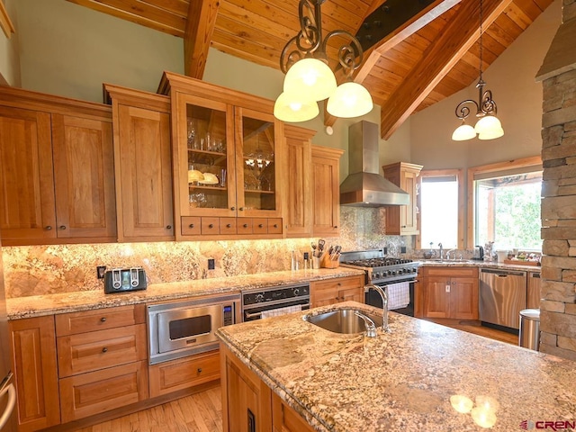 kitchen with wall chimney exhaust hood, sink, decorative light fixtures, stainless steel appliances, and light stone countertops