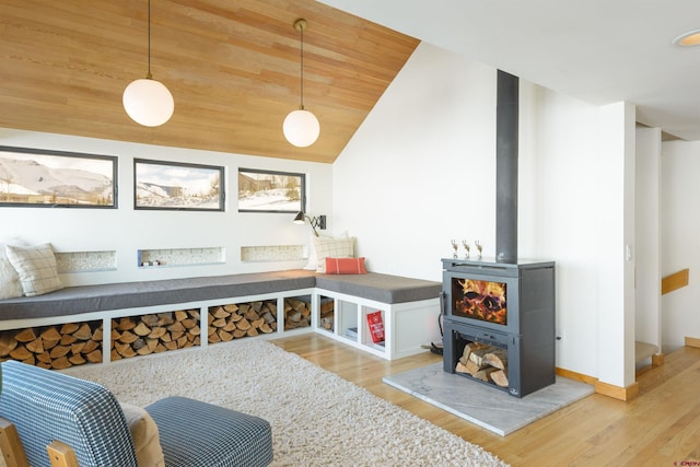 interior space with vaulted ceiling, a wood stove, wooden ceiling, and light wood-type flooring