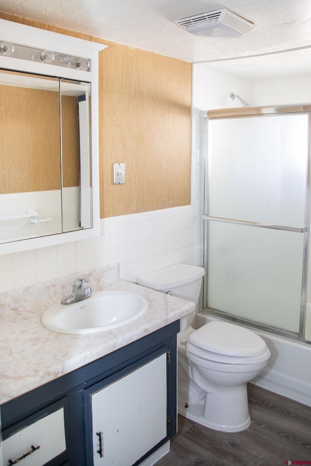 full bathroom featuring toilet, bath / shower combo with glass door, tile walls, vanity, and hardwood / wood-style flooring