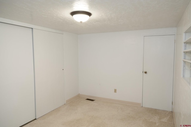 unfurnished bedroom with light colored carpet, a closet, and a textured ceiling