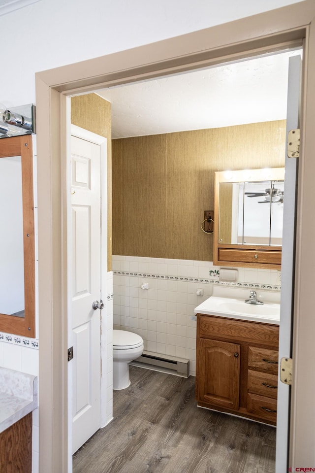 bathroom featuring hardwood / wood-style flooring, baseboard heating, tile walls, vanity, and toilet