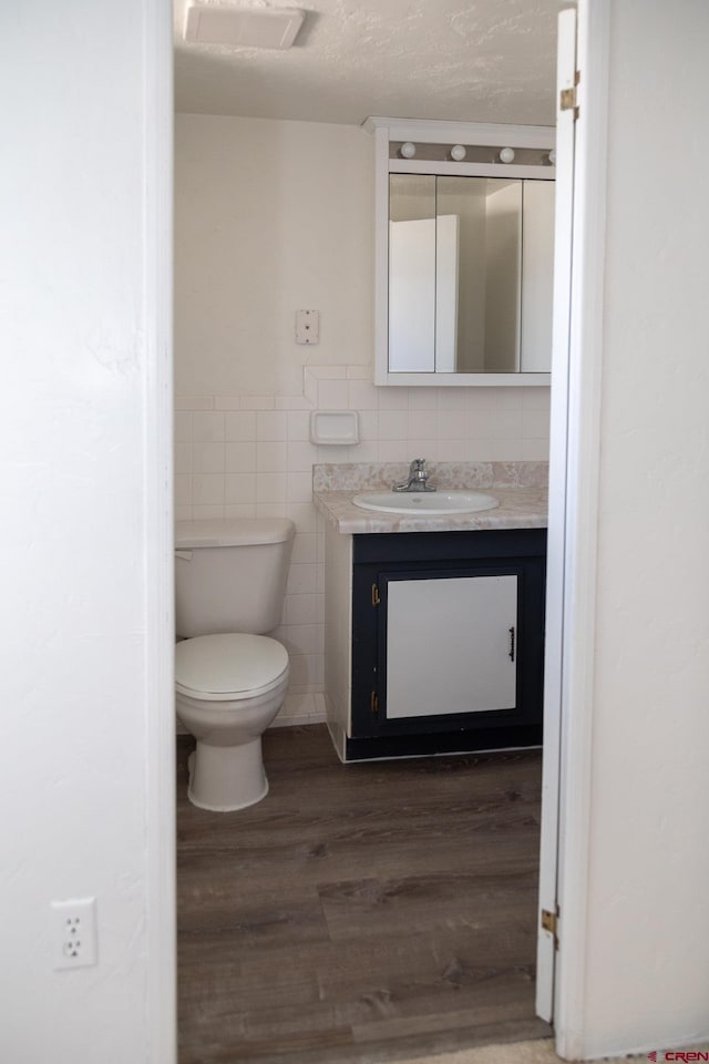 bathroom featuring toilet, tile walls, a textured ceiling, vanity, and hardwood / wood-style floors