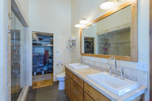 bathroom featuring tasteful backsplash, tile patterned flooring, vanity, toilet, and a shower with door