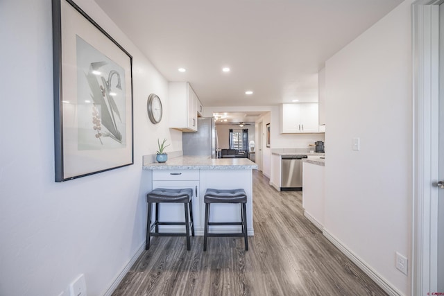 kitchen featuring appliances with stainless steel finishes, white cabinetry, a kitchen breakfast bar, kitchen peninsula, and dark wood-type flooring