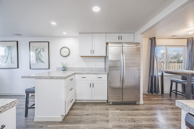 kitchen featuring wood-type flooring, stainless steel fridge, kitchen peninsula, and white cabinets