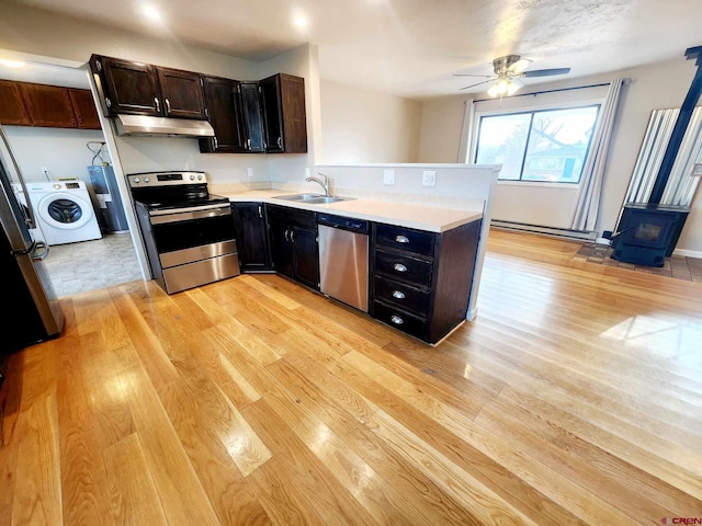 kitchen with sink, light hardwood / wood-style flooring, appliances with stainless steel finishes, washer / dryer, and a wood stove