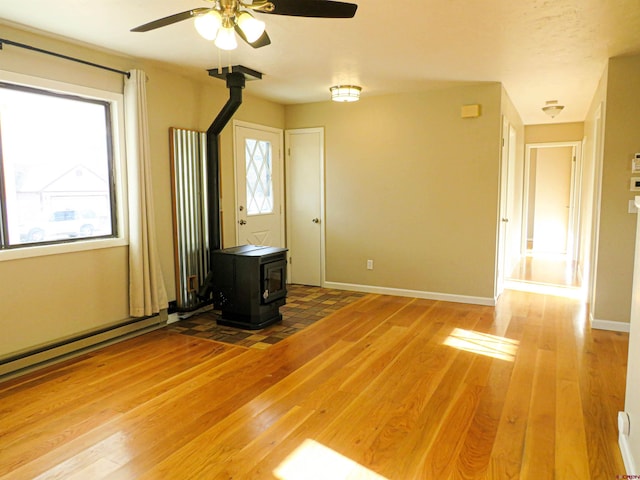 unfurnished living room with a baseboard heating unit, wood-type flooring, ceiling fan, and a wood stove