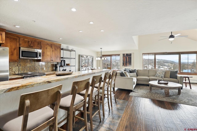 kitchen with a kitchen bar, tasteful backsplash, appliances with stainless steel finishes, dark hardwood / wood-style floors, and pendant lighting