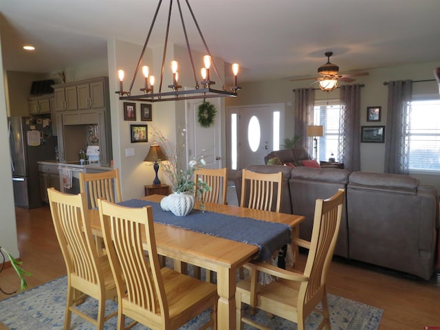 dining space with ceiling fan with notable chandelier and light wood-type flooring