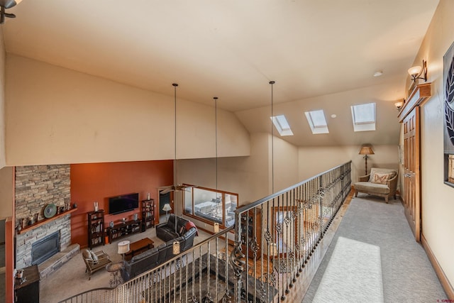 interior space with carpet, a stone fireplace, high vaulted ceiling, and a skylight