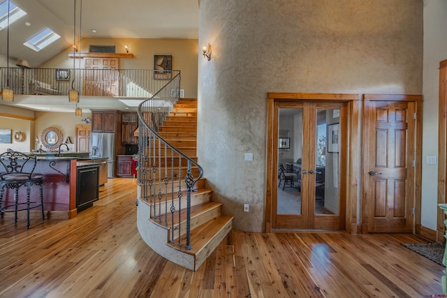 stairway featuring hardwood / wood-style floors, high vaulted ceiling, a skylight, sink, and french doors