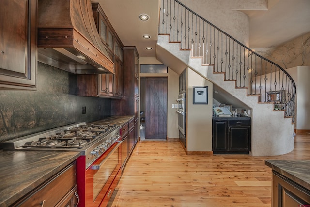 kitchen with tasteful backsplash, light hardwood / wood-style floors, stainless steel appliances, and custom range hood