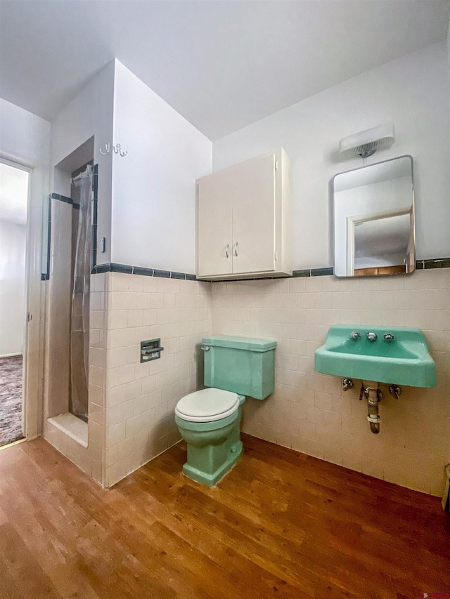 bathroom with toilet, sink, a shower, wood-type flooring, and tile walls