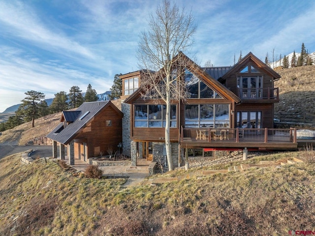 back of property with a standing seam roof, a deck, metal roof, and stone siding