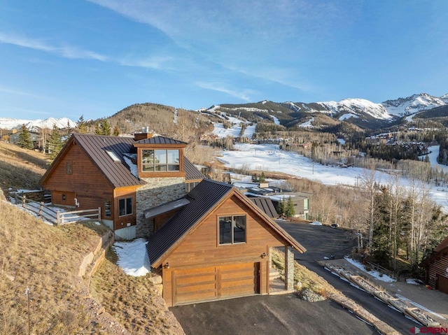 snow covered front of house with metal roof, a standing seam roof, an attached garage, and a mountain view