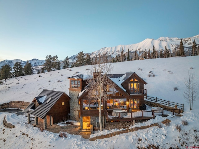 snow covered rear of property with a standing seam roof, stone siding, and a mountain view