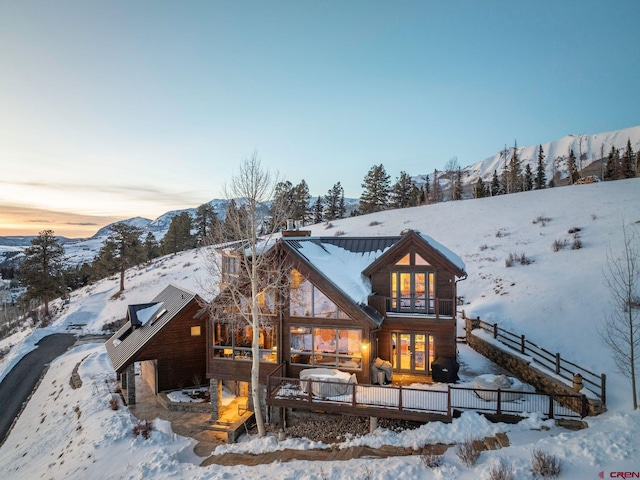 snow covered back of property featuring a garage, metal roof, a standing seam roof, and a mountain view