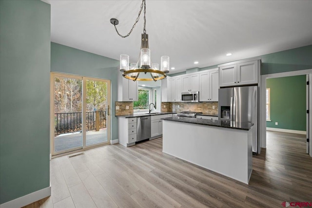 kitchen featuring sink, white cabinetry, stainless steel appliances, a center island, and decorative light fixtures