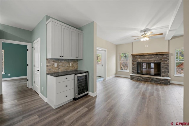 kitchen featuring wine cooler, dark wood-type flooring, a stone fireplace, white cabinetry, and tasteful backsplash