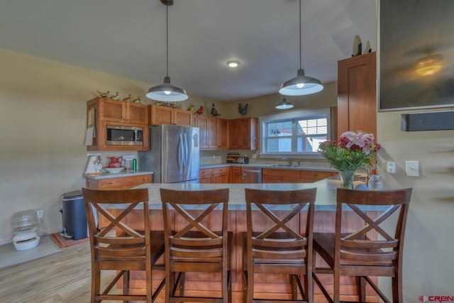 kitchen with appliances with stainless steel finishes, a breakfast bar, decorative light fixtures, kitchen peninsula, and light wood-type flooring