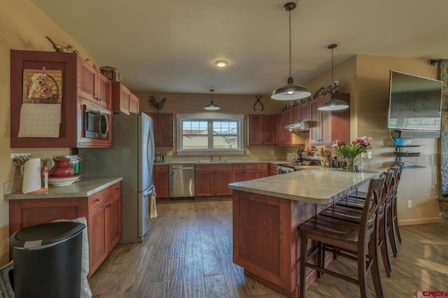 kitchen featuring sink, a breakfast bar, stainless steel appliances, dark hardwood / wood-style floors, and decorative light fixtures