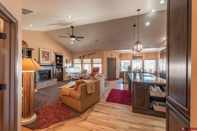 living room featuring lofted ceiling, a stone fireplace, light hardwood / wood-style flooring, and a wealth of natural light