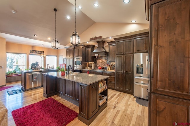 kitchen featuring custom exhaust hood, an island with sink, appliances with stainless steel finishes, and light stone countertops