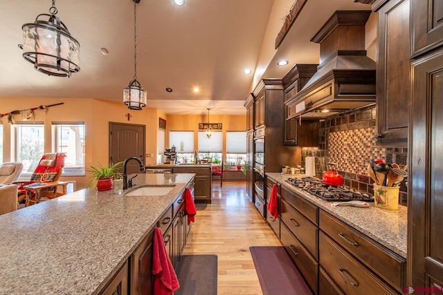 kitchen with sink, light hardwood / wood-style flooring, hanging light fixtures, light stone counters, and custom range hood