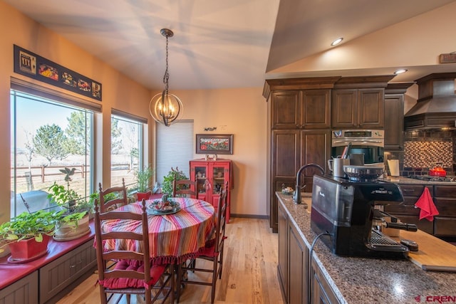 kitchen featuring premium range hood, dark brown cabinetry, dark stone countertops, pendant lighting, and oven