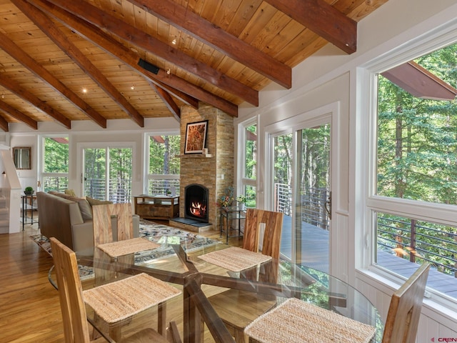 dining area with lofted ceiling with beams, a stone fireplace, hardwood / wood-style floors, and wooden ceiling