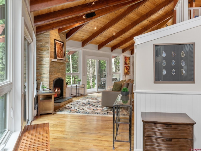 sunroom / solarium with a stone fireplace, vaulted ceiling with beams, and wooden ceiling