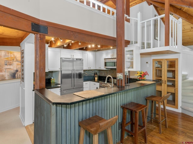 kitchen with stainless steel appliances, tasteful backsplash, white cabinets, a kitchen bar, and kitchen peninsula