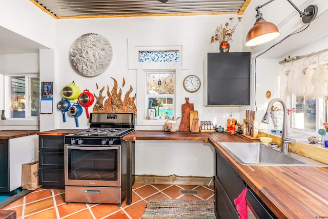 kitchen with butcher block counters, sink, decorative light fixtures, stainless steel range with gas cooktop, and plenty of natural light