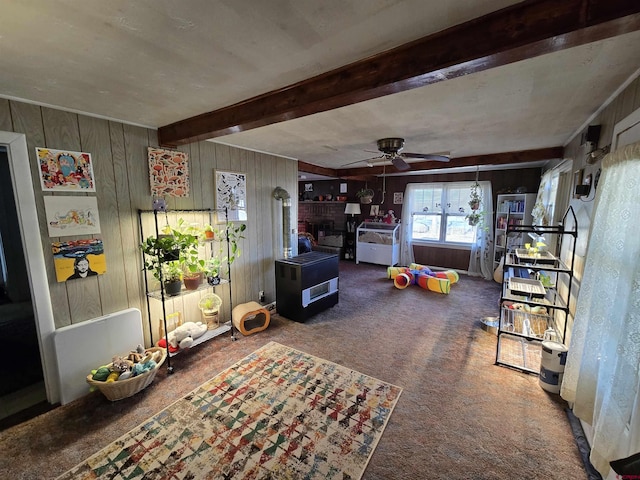 rec room featuring ceiling fan, wooden walls, carpet, a fireplace, and beamed ceiling