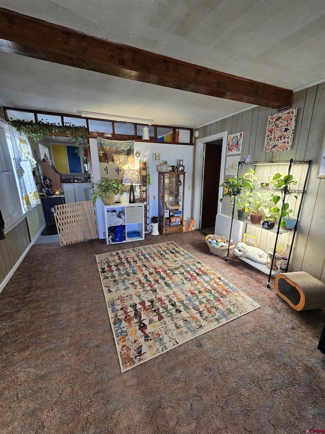 unfurnished living room featuring dark colored carpet, beam ceiling, and wood walls