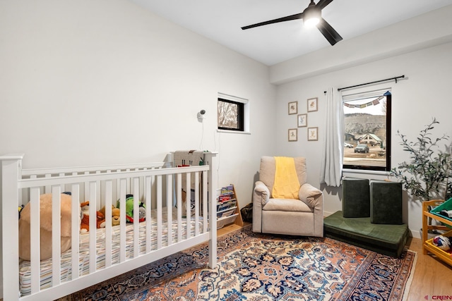 bedroom with hardwood / wood-style flooring, a nursery area, and ceiling fan