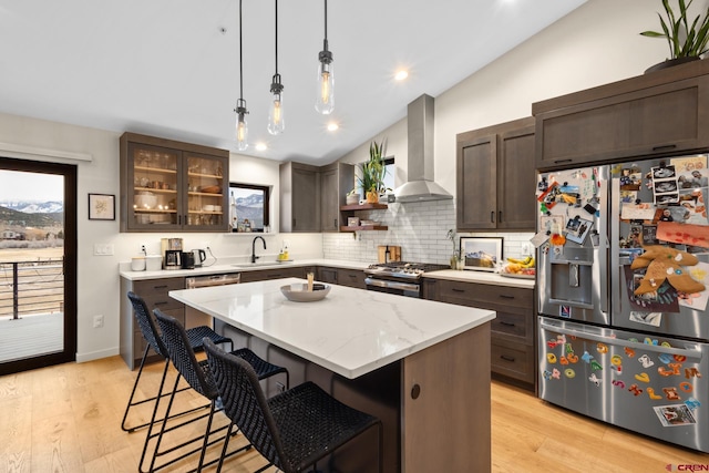 kitchen with a kitchen island, appliances with stainless steel finishes, pendant lighting, lofted ceiling, and wall chimney exhaust hood