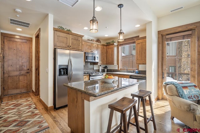 kitchen featuring decorative light fixtures, light wood-type flooring, a center island, and appliances with stainless steel finishes