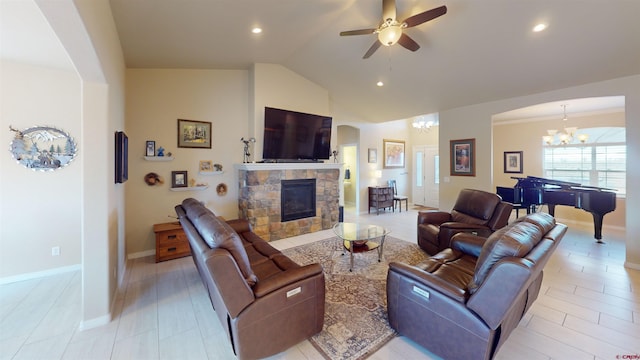 living room featuring lofted ceiling, a stone fireplace, and ceiling fan with notable chandelier