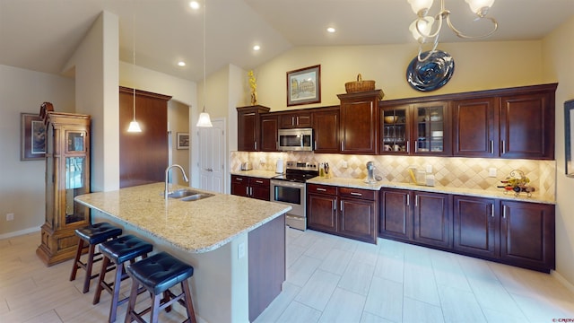 kitchen with sink, hanging light fixtures, stainless steel appliances, light stone countertops, and a kitchen bar