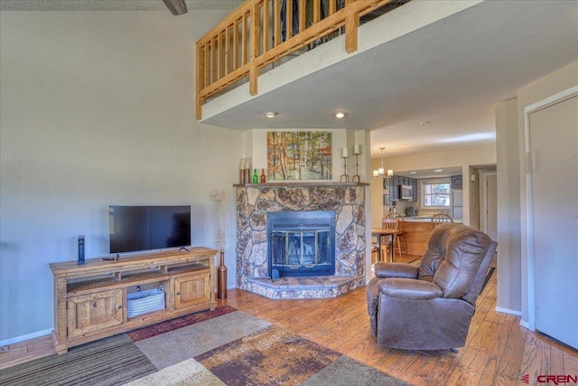 living room featuring a notable chandelier, a stone fireplace, and wood-type flooring