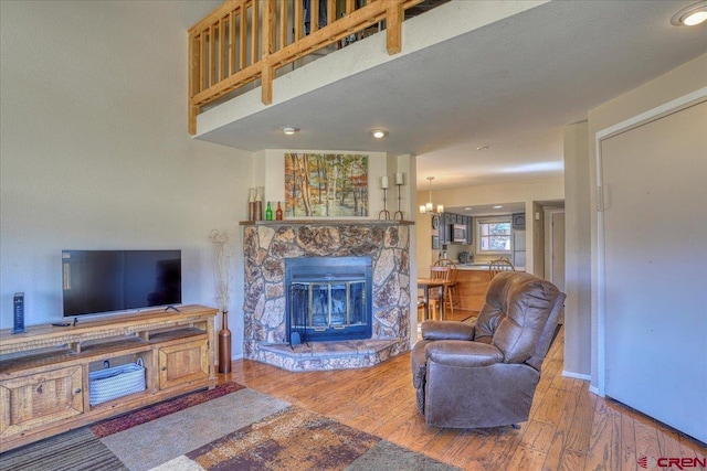 living room featuring an inviting chandelier, wood-type flooring, and a stone fireplace