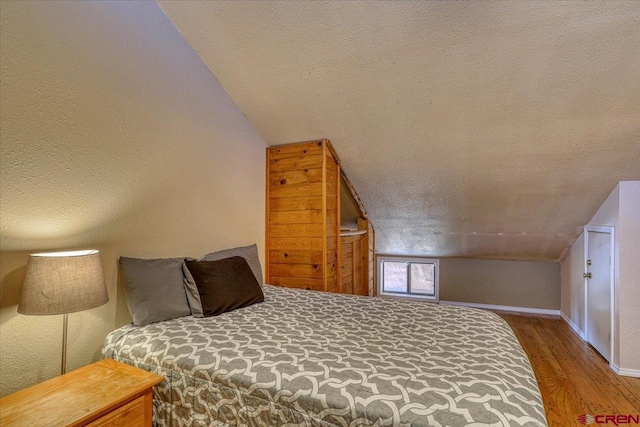 bedroom with hardwood / wood-style flooring, lofted ceiling, and a textured ceiling